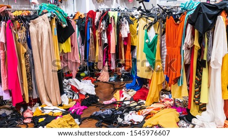 Messy clearance section in a clothing store, with colorful garments on racks and on the floor; fast fashion concept