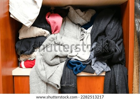 Messy closet filled with different used unfresh clothes, sloppily shoved,hanging from shelves. Fast fashion. Pile of dirty cluttered woman's wardrobe stuffed in available space,need for declutter.