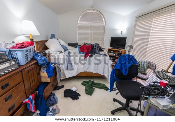 Messy, cluttered teenage boy\'s\
bedroom with piles of clothes, music and sports equipment. \
