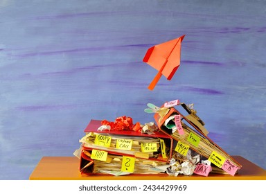 Messy file folder,sticky notes and paper plane taking off. Red tape, bureaucracy,overworked,excessive labor,burnout,exploitation,messy office and chaotic business concept.