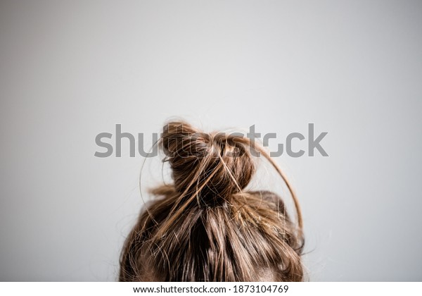 Messy hair\
bun closeup with grey white\
background.