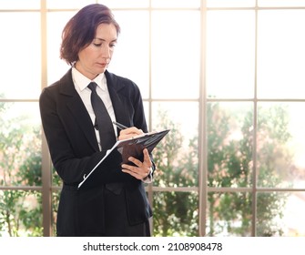 Messy Hair Businesswoman Wears Black Suit And Necktie Standing In Glass Office Wall Writing Notes. Portrait Of Beautiful Middle Aged Professional Executive Woman Busy Working Uncombed Hair Untidy Head