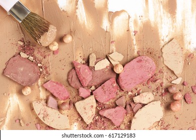 Messy Heap Of Various Crashed Face Powder, Blushers, Eyeshadow And Brush In Smudged Concealer On White Background. Neutral Colored Makeup Products. Top View Point.