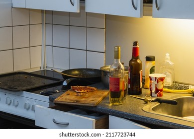 Messy Kitchen After Party. Beer Bottles, Plates In A Sink, Wine Bottle, An, Open Oven