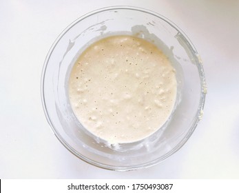 Messy mixed pancake batter in glass bowl on a white countertop background, top down view