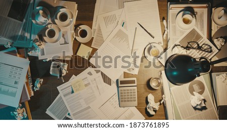 Messy office desk with paperwork and coffee cups, deadlines and business management concept, top view