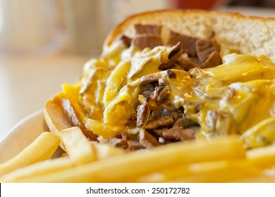 A messy Philly Cheesesteak with onions and peppers with fries on the side