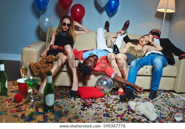 Messy room after wild house party, three\
tipsy stylish friends relaxing on couch while blond-haired woman\
with teddy bear posing for\
photography
