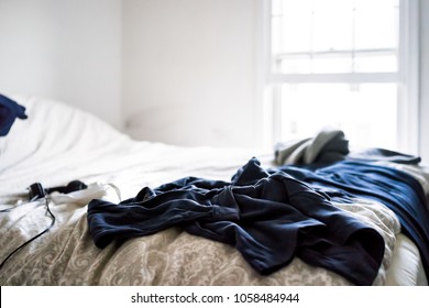 Messy Room With Dark Blue Black Clothes Lying On Top Of Bed Sheets Comforter In Depressing Cold Cool Room Closeup With Window, Headphones, Mask, Bedroom