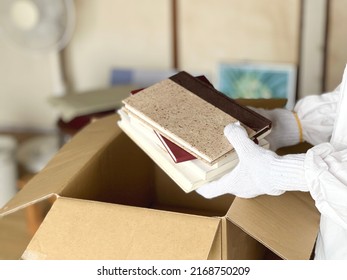A messy room with a hand that puts books etc. in a cardboard box - Shutterstock ID 2168750209