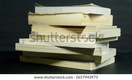 Messy stack of books with uneven alignment against black background, disorganized composition reflecting chaos, study, or unfinished work mood