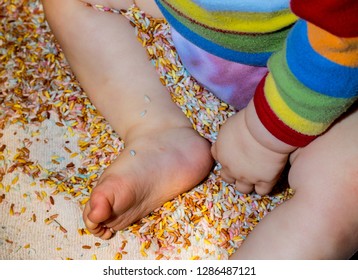 A Messy Or Tactile Play Session Where A Young Boy Or Girl In Bright Clothes Plays With Rice That Has Been Coloured To Make It More Exciting