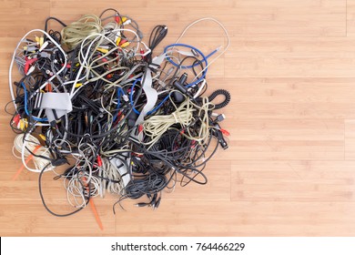 Messy tangle of old electric cords and connectors awaiting discard on a wooden surface with copy space in an overhead view