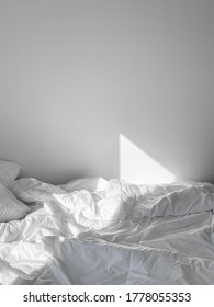 Messy Unmade Bed With All White Sheets In White Bedroom With Sun Shining In