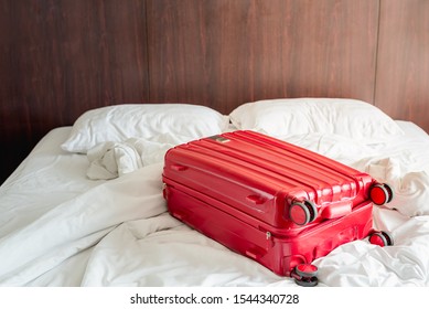 Messy And Unmade White Traveller's Hotel Bed At Hotel Room With Red Luggage.