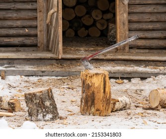 A Metal Axe Stuck In A Chopping Block, In Front Of A Firewood Storage Shed.