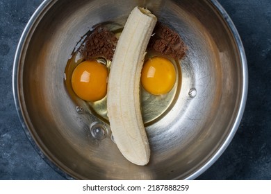 Metal Bowl With Eggs, Ripe Banana And Cocoa Powder For Making Banana Pancakes. Funny Food In The Shape Of A Face, Close-up