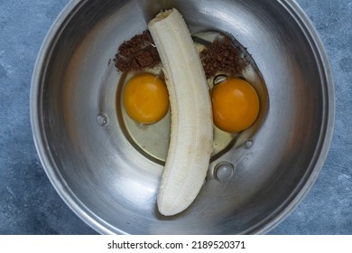 Metal Bowl With Eggs, Ripe Banana And Cocoa Powder For Making Banana Pancakes. Funny Food In The Shape Of A Face, Close-up