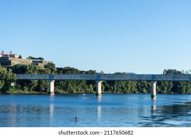 Metal Bridge Over River. Old Town In The Background. Man Kayaking In The River. High Quality Photo