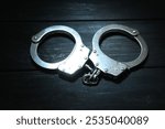 Metal chain handcuffs on black wooden table, closeup