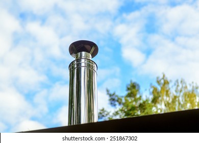 Metal Chimney On House Roof, Clean New Shiny Chimney Pipe On Blue Sky Background. Air Vent System On Home Top. Modern Round Steel Chimney On Rooftop In Summer Close-up.