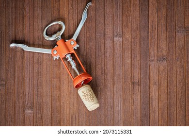 Metal Corkscrew With A Cork Cork Of Extracted Wine Is Resting On A Wooden Table, View From Above, Ample Free Space For Text.