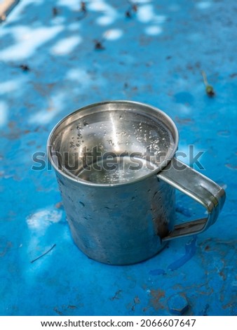 Metal cup filled with water. Water in a cup. Blue painted metal table. United States