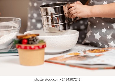 Metal cup sieve in the hands of a child, sifting flour, the process of making dough at Christmas. - Powered by Shutterstock