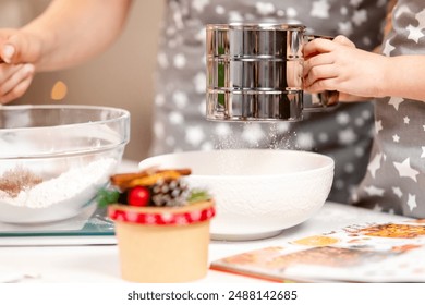 Metal cup sieve in the hands of a child, sifting flour, the process of making dough at Christmas with adult. - Powered by Shutterstock