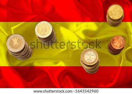 metal currency coins against the background of the national flag of Spain, the concept of financial development, devaluation, inflation, taxes