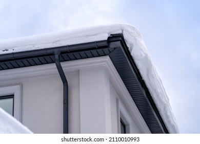 Metal Downpipe system, Guttering System, External downpipes and drainage pipes under snow. Corner of house with roof made of gray metal tiles and gutter covered with thick layer of snow in winter.