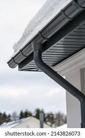 Metal Downpipe system, Guttering System, External downpipes and drainage pipes under snow. Corner of house with roof made of gray metal tiles and gutter covered with thick layer of snow in winter.