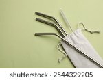 Metal drinking straws and cleaning brush on green background, top view. Space for text