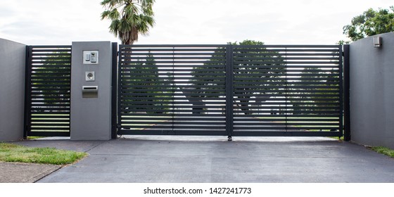 Metal driveway property entrance gates set in concrete fence with garden trees  in background - Shutterstock ID 1427241773