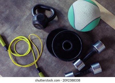 Metal Dumbbells, Barbell Discs, Kettlebell, Skipping Rope And Medicine Ball On The Gym Floor. Fitness, Bodybuilding And Functional Training Equipment