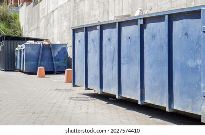 Metal durable blue industrial trash bin for outdoor trash at construction site. Large waste basket for household or industrial waste. A pile of waste