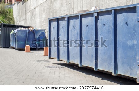 Metal durable blue industrial trash bin for outdoor trash at construction site. Large waste basket for household or industrial waste. A pile of waste