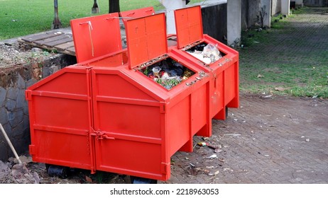 Metal Durable Orange Industrial Trash Bin For Outdoor Trash At Construction Site. Large Waste Basket For Household Or Industrial Waste. A Pile Of Waste