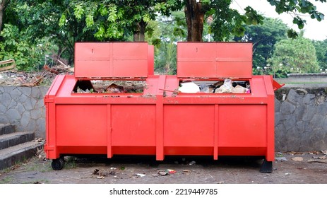 Metal Durable Orange Industrial Trash Bin For Outdoor Trash At Construction Site. Large Waste Basket For Household Or Industrial Waste. A Pile Of Waste