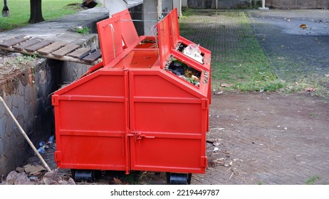 Metal Durable Orange Industrial Trash Bin For Outdoor Trash At Construction Site. Large Waste Basket For Household Or Industrial Waste. A Pile Of Waste