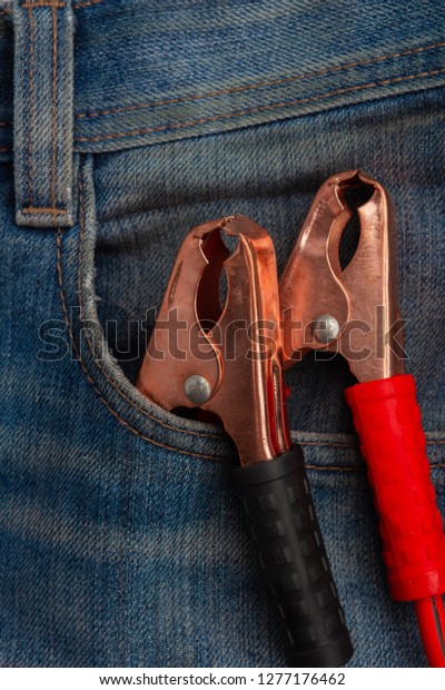 metal electric red and black clamps for\
emergency car start in blue jeans pocket\
closeup