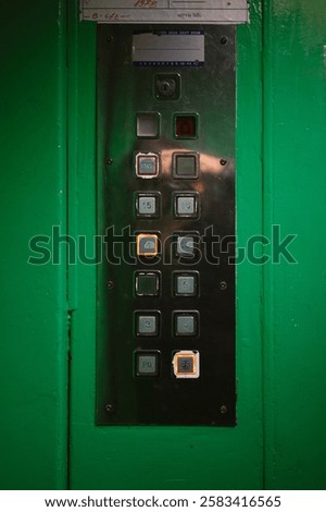 Metal elevator control panel with floor selection buttons, the eleventh floor is selected. The elevator cabin is green.