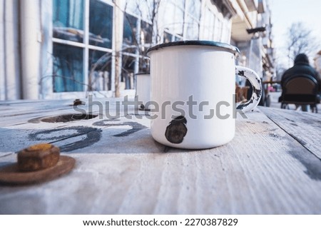A metal enamalized mug stands on a table of unstrung boards in the middle of the street