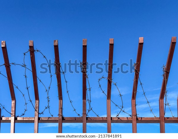 Metal\
fence with barbed wire on its top against blue\
sky