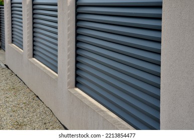 metal fillings of the fence with an underlay of concrete blocks. A metal aluminum fence will provide privacy around the garden. horizontal slats cover well. a hedge made of tuji adds protection - Shutterstock ID 2213854477