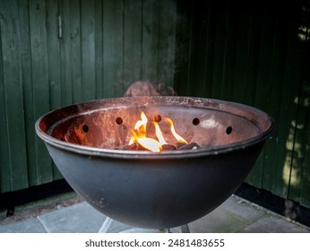 Metal Fire Pit with Flames Against Green Wooden Wall - Powered by Shutterstock