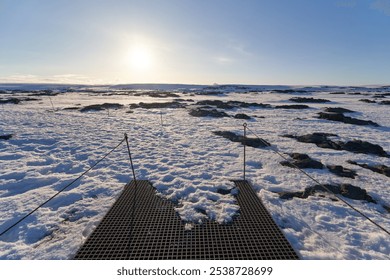 Metal footbridge with safety cables is leading through a snow covered landscape in iceland during sunset - Powered by Shutterstock