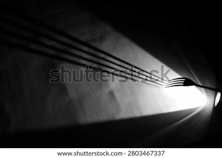 A metal fork with dramatic spotlight, forming a curved silhouette and sharp shadow on white surface, black background, high-contrast monochrome still life.