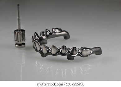 a metal frame of a dental prosthesis, on a gray background with a dental screwdriver
