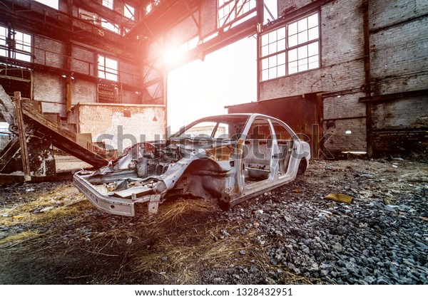Metal frame of a rusty car in\
a big old abandoned building inside with light leaks. Broken and\
forgotten rusted car frame on the background of ruined\
plant